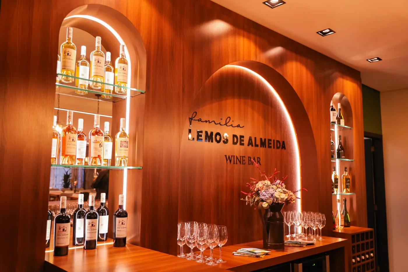 Balcão do Wine Bar sob o arco iluminado, com as garrafas e as taças